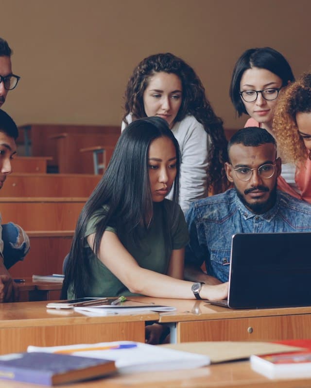 Students gathered around a laptop in a lecture hall