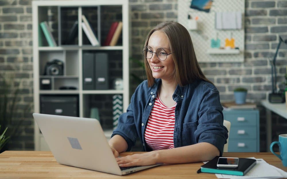 A smiling professional working on a laptop at a bright office desk