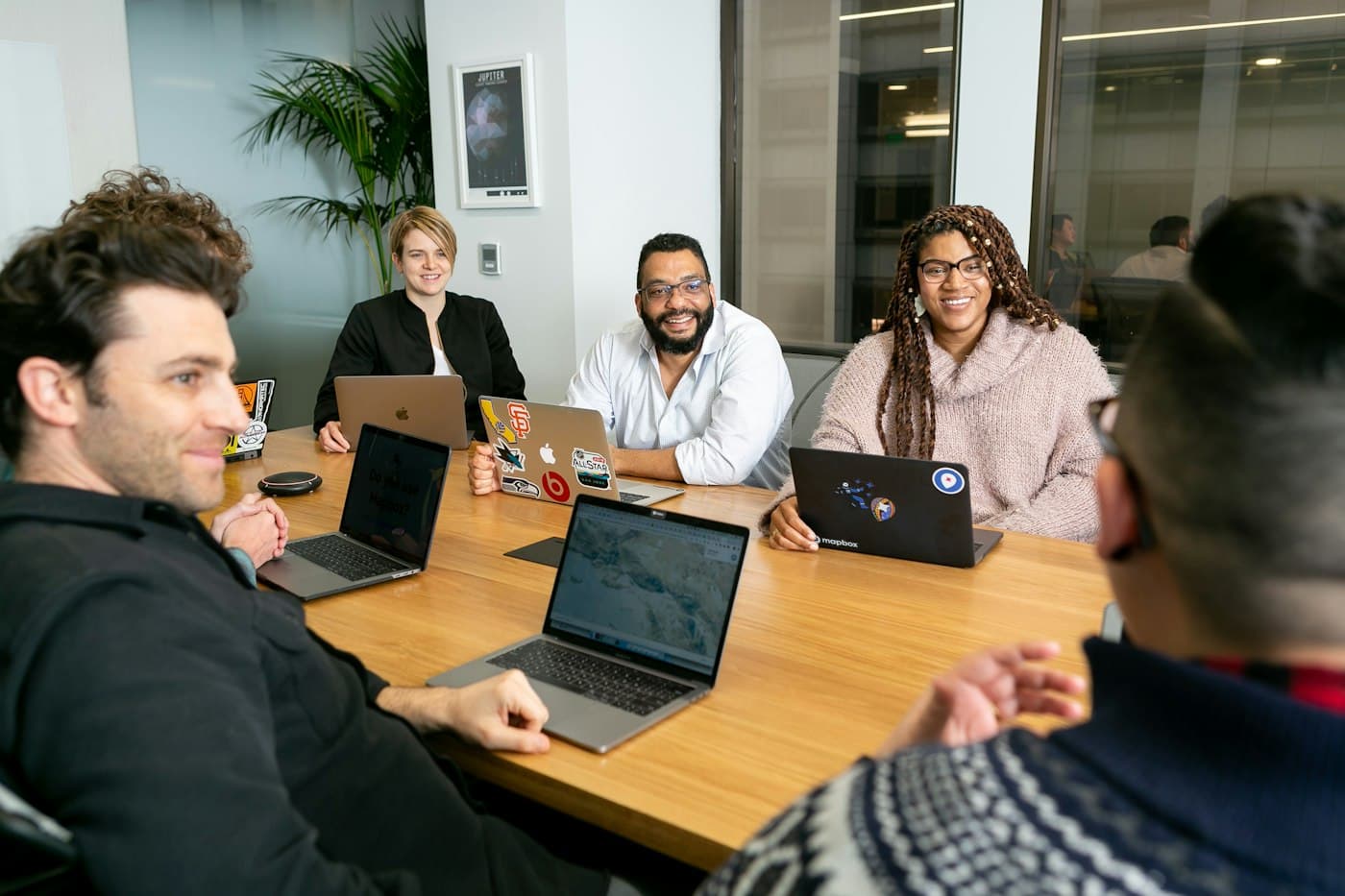 A team meeting around a long table with laptops open